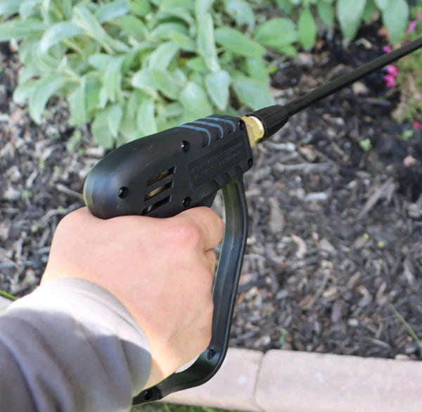 Hand holding a black pressure washer gun with garden in the background